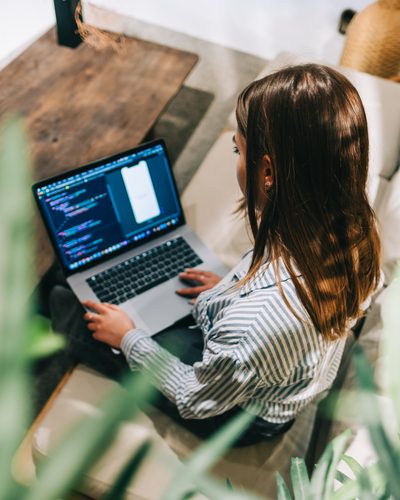 Young woman mobile developer with laptop, writes program code on a computer, programmer work in modern office.